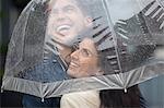 Happy couple under umbrella looking up at rain