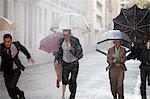 Enthusiastic business people with umbrellas running in rainy street