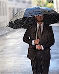 Happy businessman with umbrella walking in rainy street