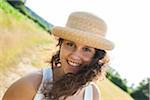 Close-up portrait of teenaged girl standing in field, wearing straw hat, smiling at camera, Germany