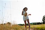 Teenaged girl holding straw hat and walking in field on summer day, Germany