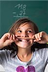 Portrait of girl standing in front of blackboard in classroom, holding pencil over mouth, Germany