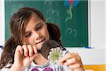 Girl in classroom examining flower with magnifying glass, Germany