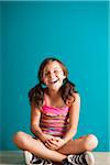 Portrait of girl sitting on floor, laughing, Germany