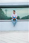 Young man sitting on ledge outdoors, Germany