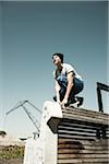 Teenager crouching down on barrier, anticipating next move, freerunning, Germany