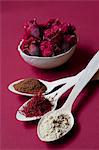 Spoons of liquorice root powder, saffron threads and cinnamon, with a bowl of pomegranate flowers