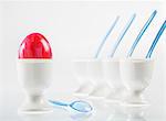 An egg, coloured red for Easter, next to a row of white eggcups