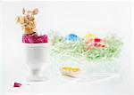 An Easter bunny figurine in a boiled egg with the top cut off, with an Easter nest of colourful eggs in the background