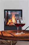 Two glasses of red wine on a table in front of a fireplace