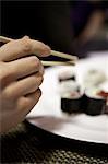 A hand reaching for a piece of sushi using chopsticks