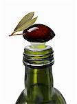 A black olive on top of an olive oil bottle