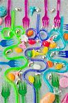 graphic overview of coloured plastic party forks and blue and purple curved drinking straws on a silver glittery background with sweets