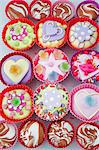 overview o of coloured cup cakes in red and pink plastic cake covers decorated with hearts, lips and sweets