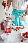 Strawberry compote being spooned into a preserving jar