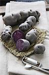 Violet truffle potatoes, whole and halved, with a potato peeler