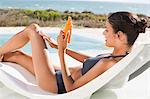 Beautiful woman applying suntan lotion while sunbathing on the beach