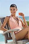 Beautiful woman holding a glass of juice and sitting on a chair on the beach