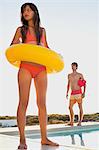 Woman walking with inflatable ring at the poolside with a man behind her