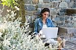 Woman leaning against a stone wall and using a laptop
