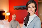 Portrait of a woman smiling in a hotel room with her husband in the background