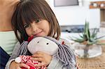 Close-up of a girl sitting with her mother and holding a rag doll