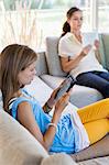 Girl using a digital tablet with her mother reading book at home