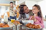 Girl having breakfast beside her mother at a kitchen counter