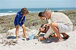 Children playing in sand with their grandfather on the beach