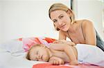 Woman sitting near her baby sleeping on the bed