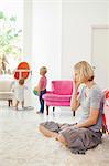 Woman sitting on a rug with her children playing in the background