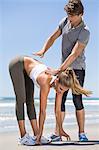 Man helping woman stretch at beach