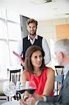 Couple enjoying red wine in a restaurant with waiter in the background