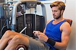 Man sitting on an exercise machine and using a mobile phone in a gym