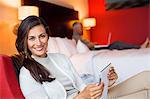 Woman using a digital tablet in a hotel room with her husband using laptop in the background