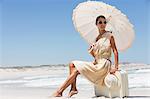 Beautiful woman sitting on a suitcase with an umbrella on the beach