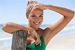 Smiling woman leaning against a wooden post on the beach