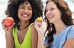 Close-up of two smiling female friends eating fruits