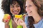Close-up of two smiling female friends eating fruits