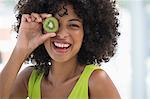 Smiling woman holding a kiwi fruit in front of her eye