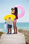 Woman with her children holding inflatable rings on a boardwalk on the beach