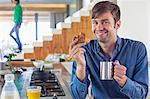 Man having breakfast at a kitchen counter with his wife in the background