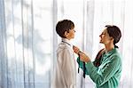 Mother tying son's tie at window