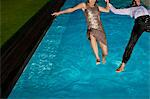 Fully dressed couple jumping into swimming pool