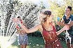 Friends playing with water guns in sprinkler