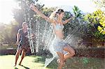 Couple playing in sprinkler in backyard