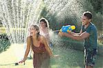 Friends playing with water guns in sprinkler in backyard