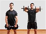 Personal Trainer doing front dumbell raises for training his deltoids, in a gym