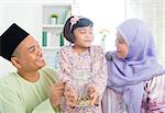 Islamic banking concept. Southeast Asian Malay family saving money at home. Muslim father, mother and daughter living lifestyle.