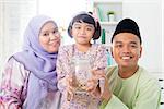 Southeast Asian Malay family saving money at home. Muslim father, mother and daughter living lifestyle. Islamic banking concept.